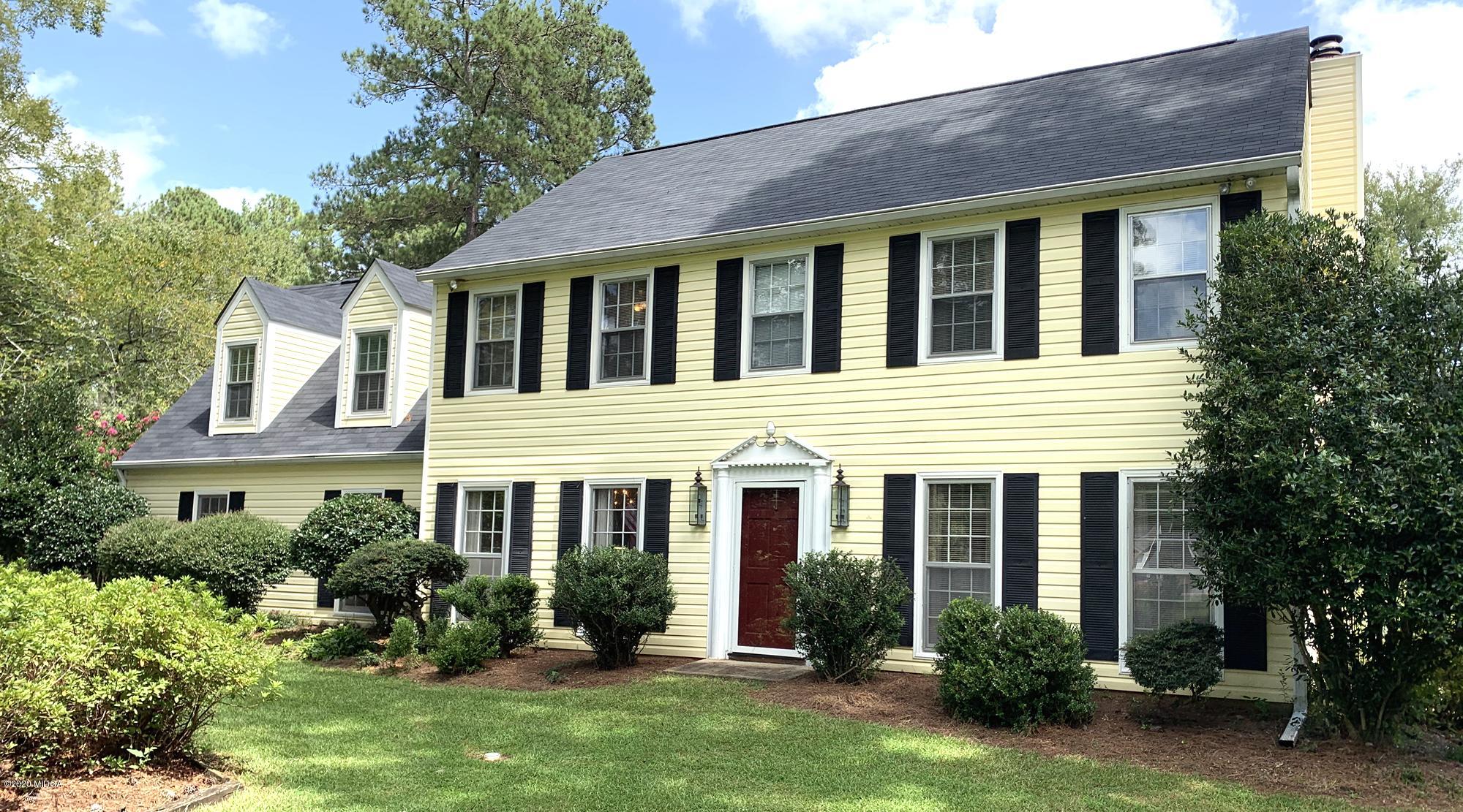 front view of a brick house with a yard and large trees