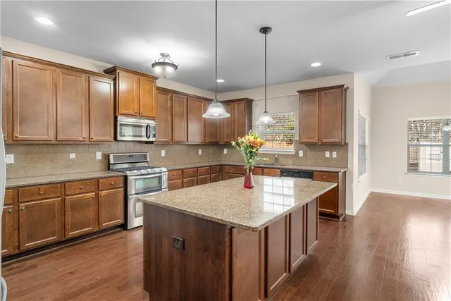 a kitchen with kitchen island granite countertop wooden cabinets a sink a center island and stainless steel appliances