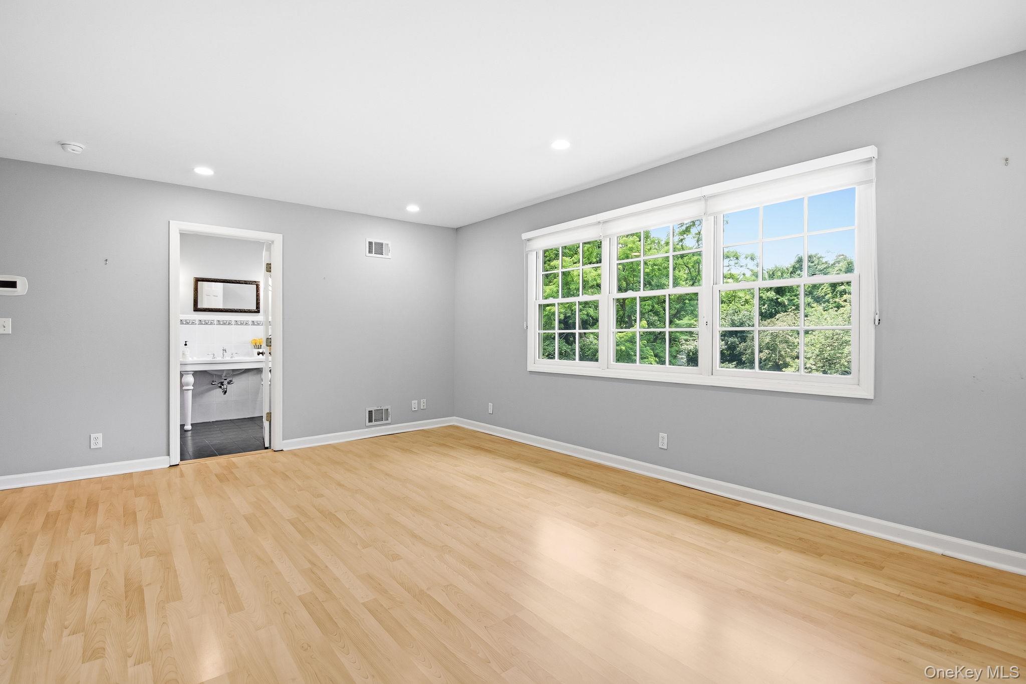 26 Century Ridge Road Purchase, NY 10577 - Photo 16 of 50 Primary en-suite (split level up); bright room featuring extensive natural light from multiple windows, recessed ceiling lighting, light wood-finish flooring, and light gray walls; alternate view towards primary bathroom.