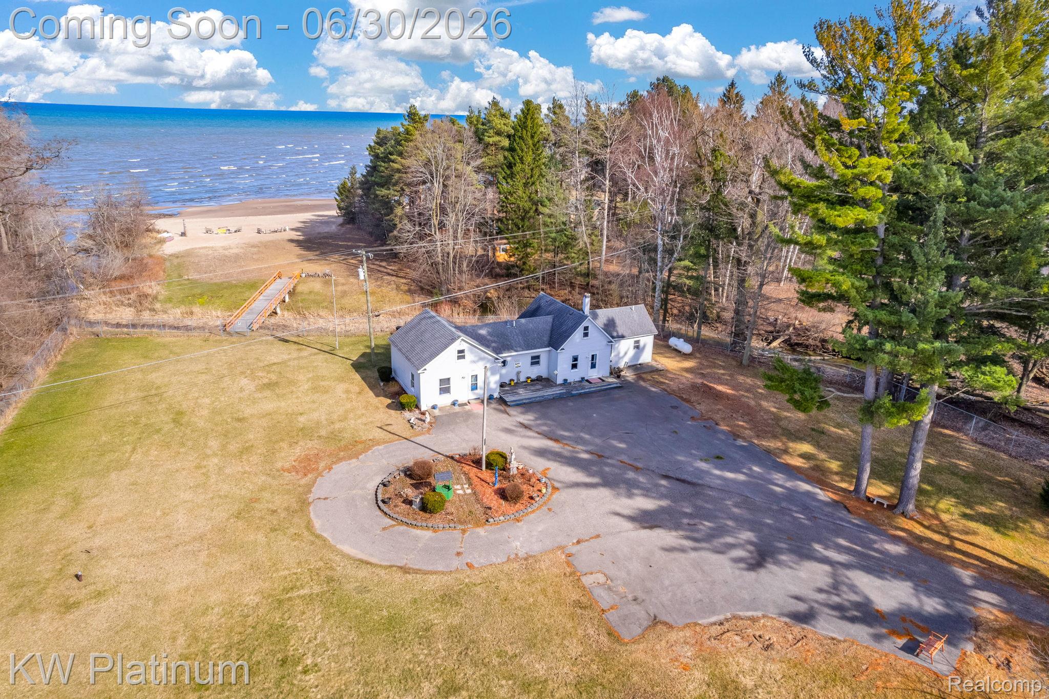 2235 South Lake Shore Road Harbor Beach, MI 48441 - Photo 57 of 99 Waterfront property featuring a white residence with dark roof, expansive paved driveway with a central landscaped island, generous green space, and mature trees framing the perimeter