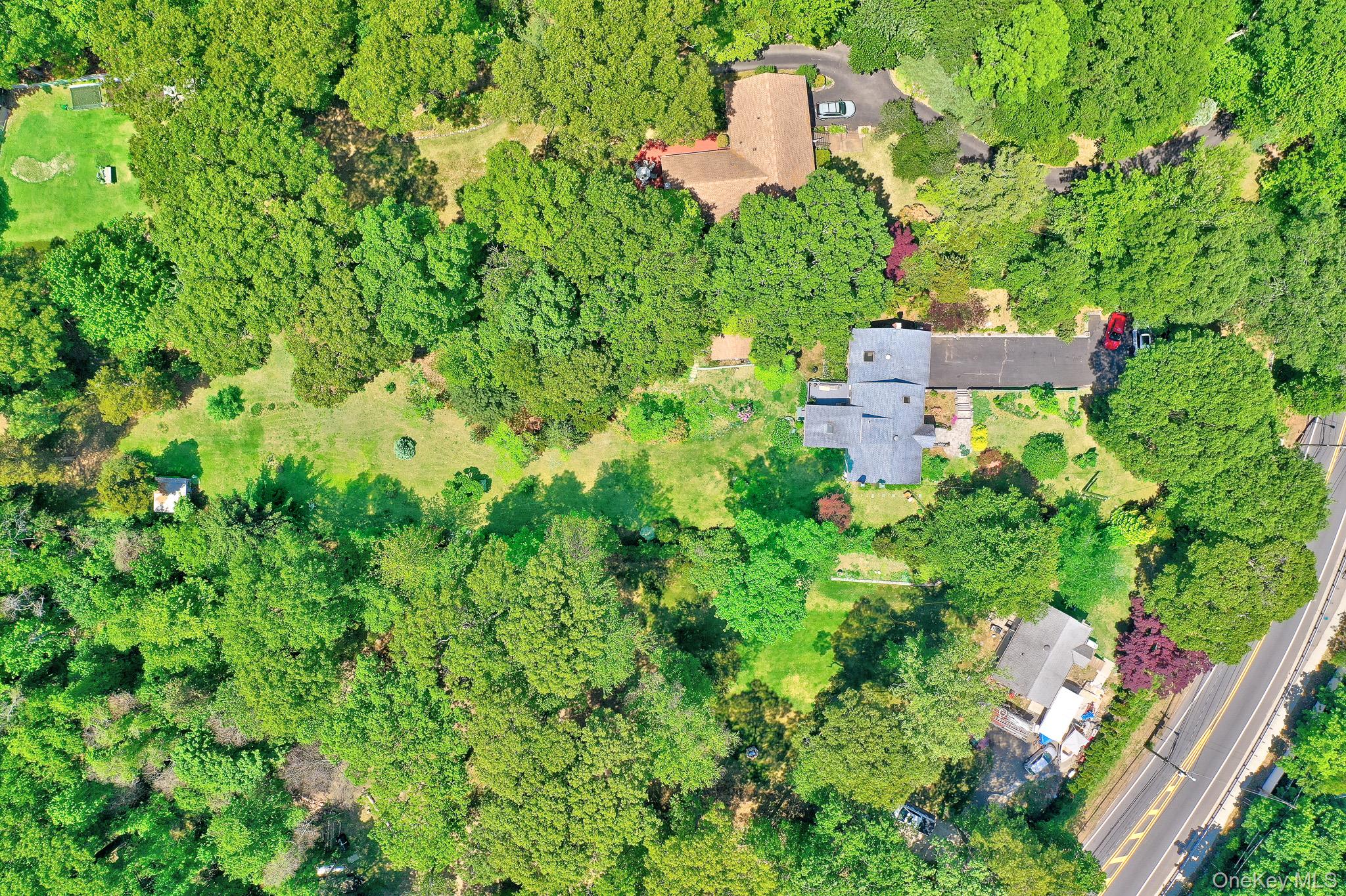 100 Elwood Road Northport, NY 11768 - Photo 29 of 39 Extensive tree canopy surrounding a property featuring a multi-level roofline, a paved driveway, and a manicured lawn area