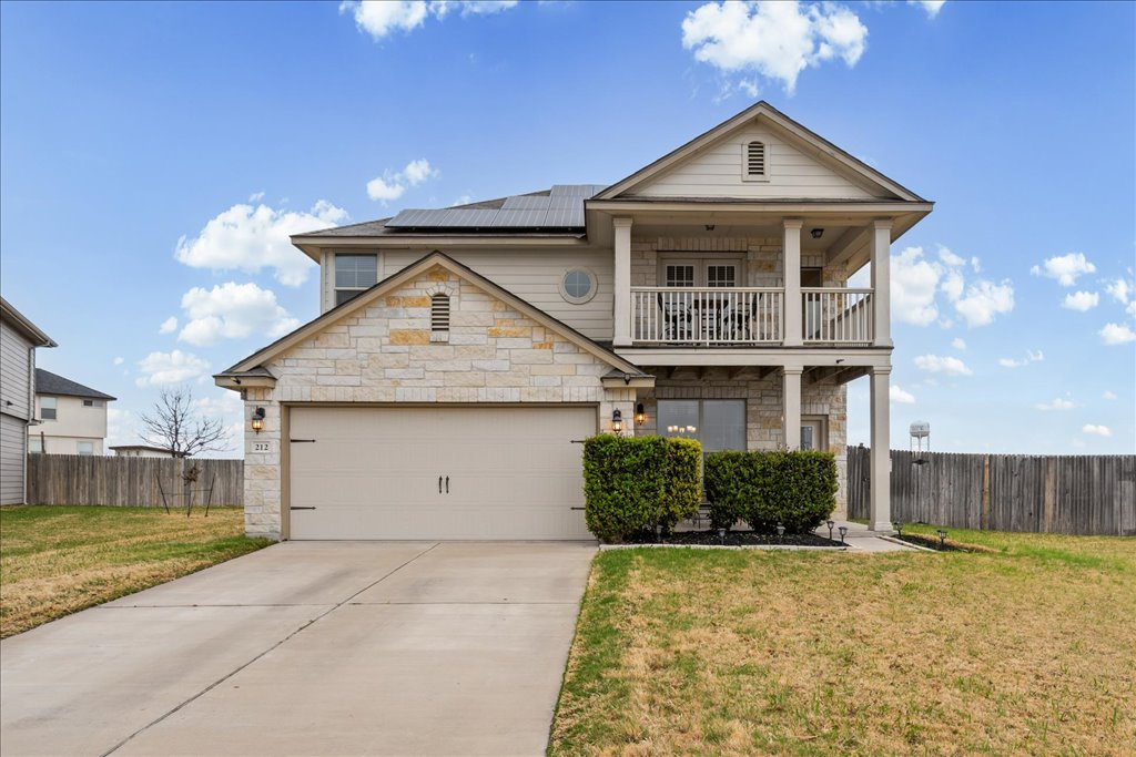 View of front facade featuring solar panels, stone siding, a garage, a balcony, and concrete driveway