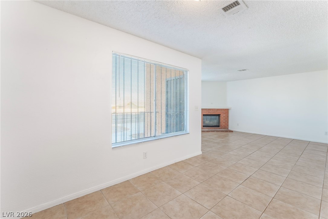 2257 Exeter Drive, Unit B Las Vegas, NV 89156 - Photo 16 of 39 Unfurnished living room featuring a brick fireplace, a textured ceiling, and light tile patterned floors