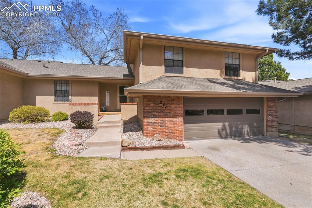 The property features a stucco exterior with brick accents, a gray asphalt shingle roof, and an attached garage with a paved driveway