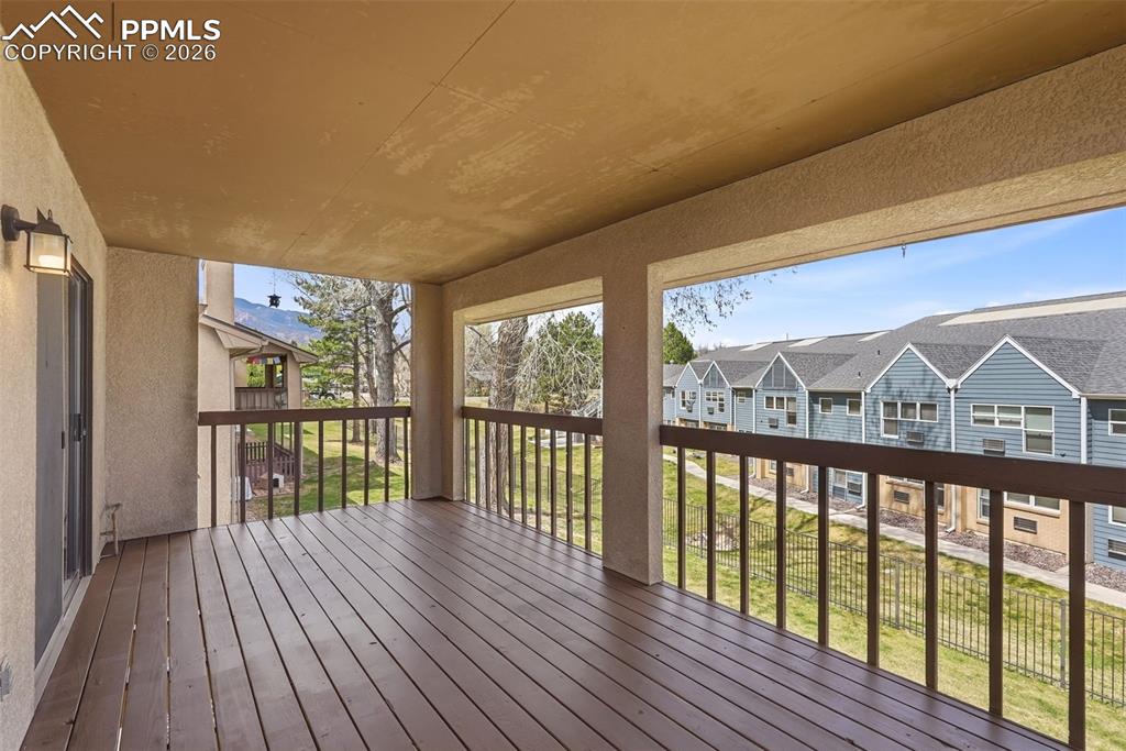 240 Bennington Drive Colorado Springs, CO 80906 - Photo 12 of 44 Covered outdoor deck with wood flooring and dark wood railings, offering views of distant mountains and surrounding properties
