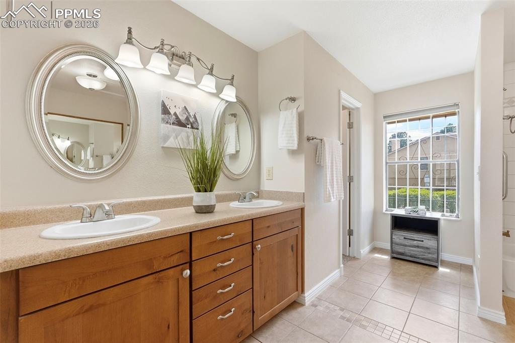 240 Bennington Drive Colorado Springs, CO 80906 - Photo 19 of 44 The bathroom features a double vanity with light wood cabinetry, two oval mirrors, and a tiled floor