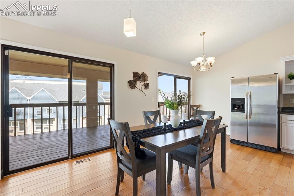 240 Bennington Drive Colorado Springs, CO 80906 - Photo 6 of 44 Dining area with hardwood floors, a sliding glass door leading to a deck, and an open concept view of the kitchen area featuring a stainless steel refrigerator