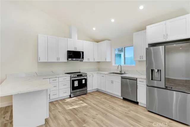 a view of an empty room and kitchen with wooden floor