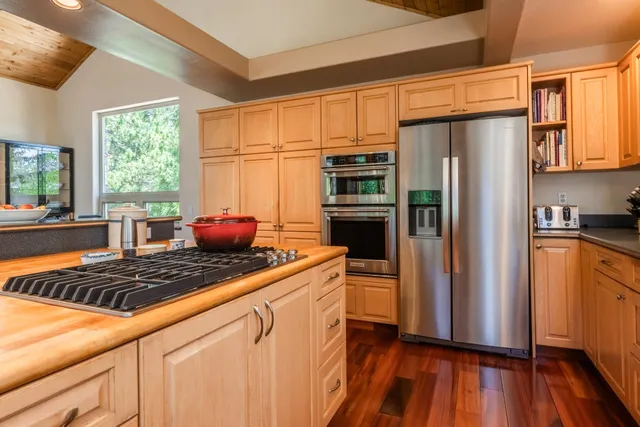 a kitchen with stainless steel appliances a refrigerator a sink a stove and white cabinets with wooden floor