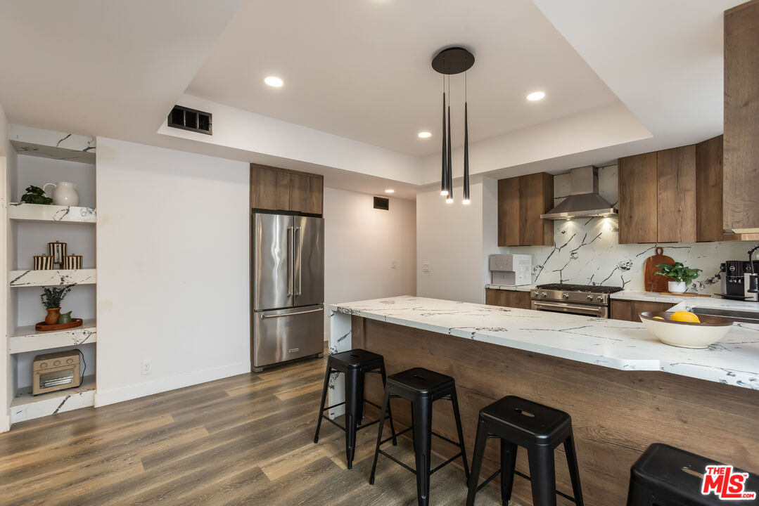1210 North Kings Road, Unit 101 West Hollywood, CA 90069 - Photo 18 of 32 a kitchen with stainless steel appliances granite countertop a refrigerator a sink dishwasher a stove and white countertops with wooden floor