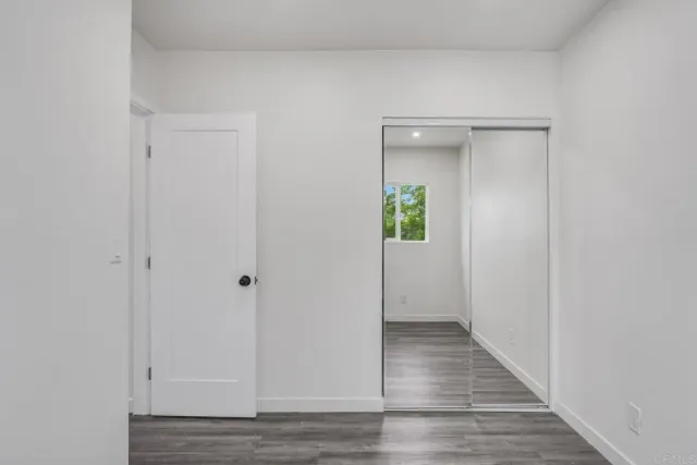 a view of an empty room with wooden floor and a mirror