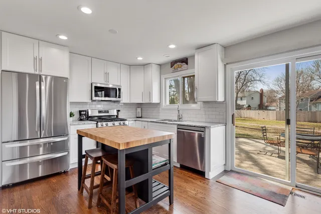 a kitchen with kitchen island granite countertop a stove top oven a sink dishwasher a refrigerator and white cabinets with wooden floor