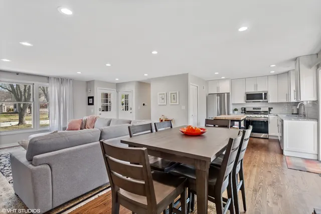 a view of a dining room and livingroom with furniture wooden floor a rug a kitchen view and a chandelier