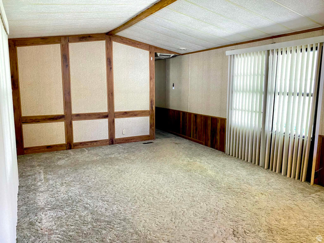 1111 North 2000 West, Unit 147 Ogden, UT 84404 - Photo 5 of 12 Spacious room featuring textured carpeting, a window with vertical blinds, and a paneled accent wall with wood-finish trim and wainscoting