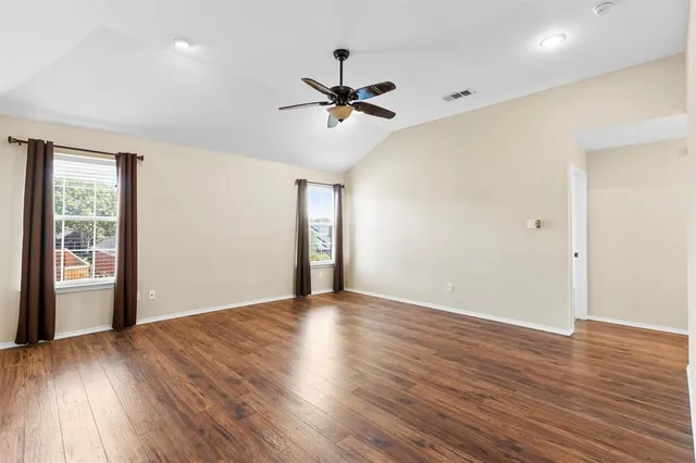 an empty room with wooden floor a ceiling fan and windows