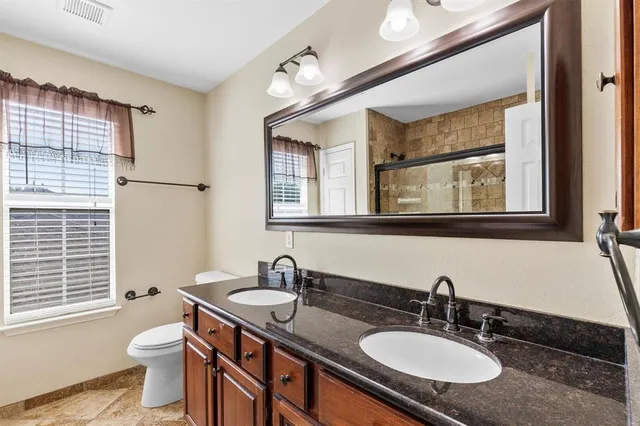 a bathroom with a granite countertop sink a toilet a mirror and a window