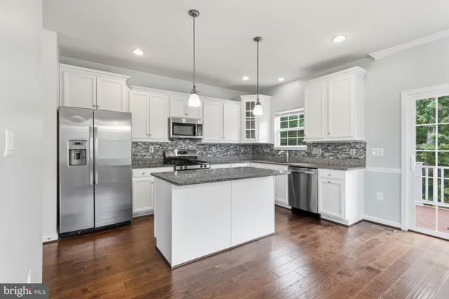 a kitchen with stainless steel appliances granite countertop a refrigerator a sink dishwasher a stove and white cabinets with wooden floor