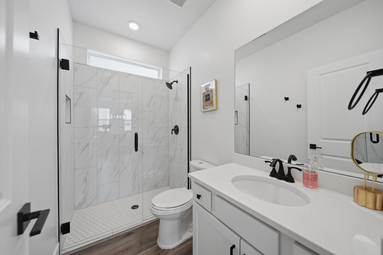 6144 Red Sand Lane St. George, UT 84790 - Photo 15 of 19 Clean lines define this well-appointed bath, where a glass-enclosed shower wrapped in marble-patterned tile pairs with a quartz-topped vanity and oil-rubbed bronze fixtures. Thoughtful recessed lighting, a tucked-away toilet closet, and warm wood-look flooring keep the layout both private and practical for daily routines.