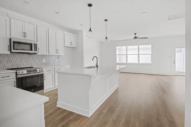 a kitchen with stainless steel appliances white cabinets a sink a stove a microwave and wooden floors