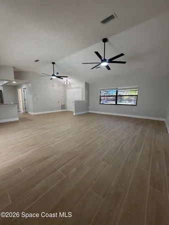 an empty room with wooden floor ceiling fan and windows