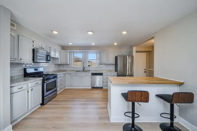 a kitchen with stainless steel appliances granite countertop a stove top oven a sink dishwasher a refrigerator and white cabinets with wooden floor