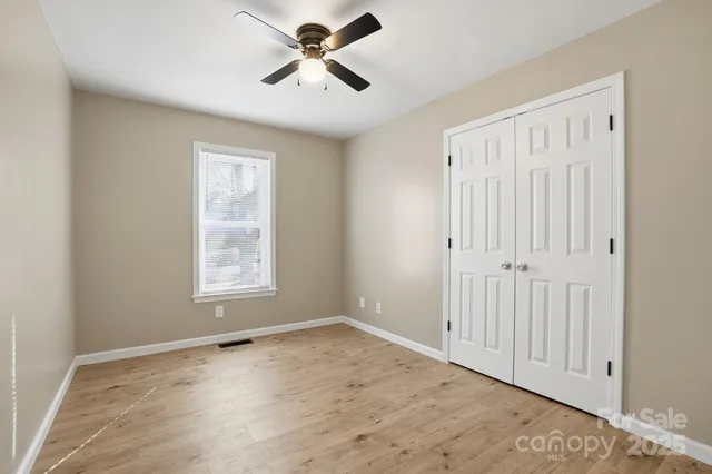 an empty room with wooden floor ceiling fan and windows