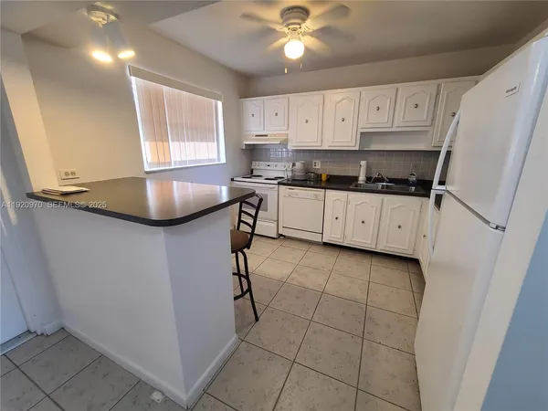 a kitchen with granite countertop a sink a stove a refrigerator cabinets and a window