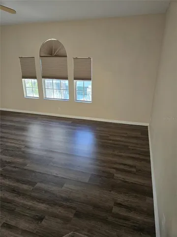 an empty room with wooden floor chandelier fan and windows