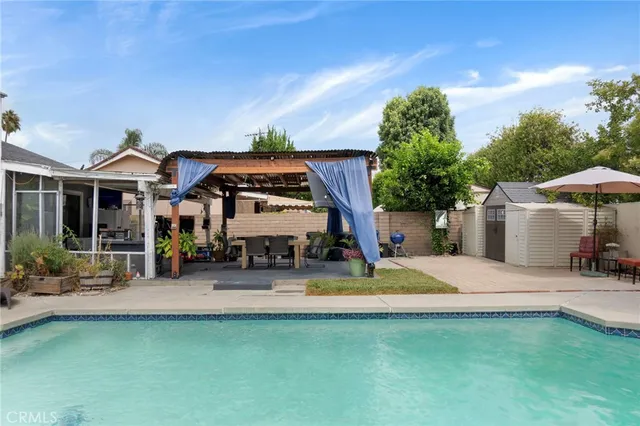 an outdoor view of a swimming pool with a table and chairs under an umbrella