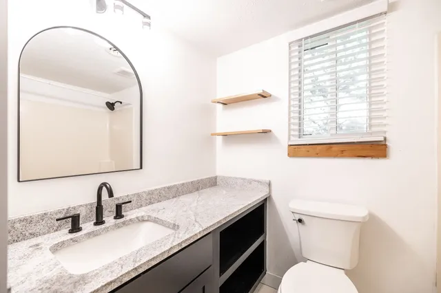 a bathroom with a granite countertop sink toilet and mirror