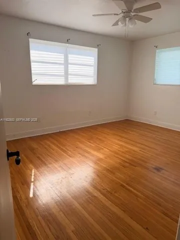 an empty room with wooden floor fan and windows