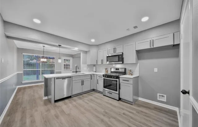 a kitchen with stainless steel appliances granite countertop a stove top oven a sink dishwasher a refrigerator and white cabinets with wooden floor