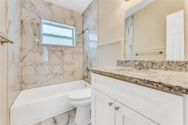 a bathroom with a granite countertop bathtub sink mirror and toilet