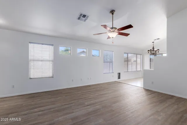 an empty room with wooden floor ceiling fan and windows