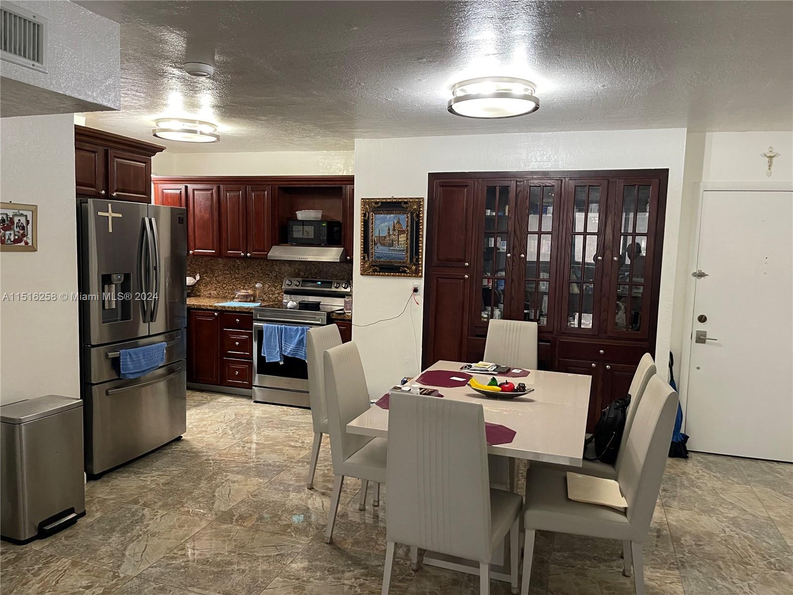 a kitchen with stainless steel appliances kitchen island granite countertop a refrigerator a stove a microwave oven a dining table and chairs with wooden floor