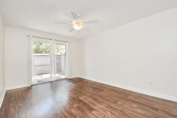 an empty room with wooden floor chandelier fan and windows