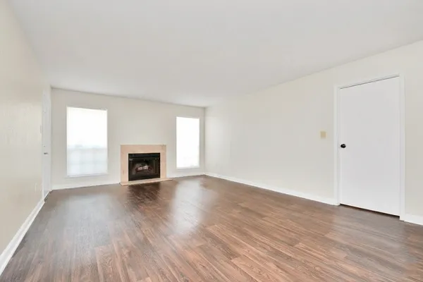 an empty room with wooden floor fireplace and windows