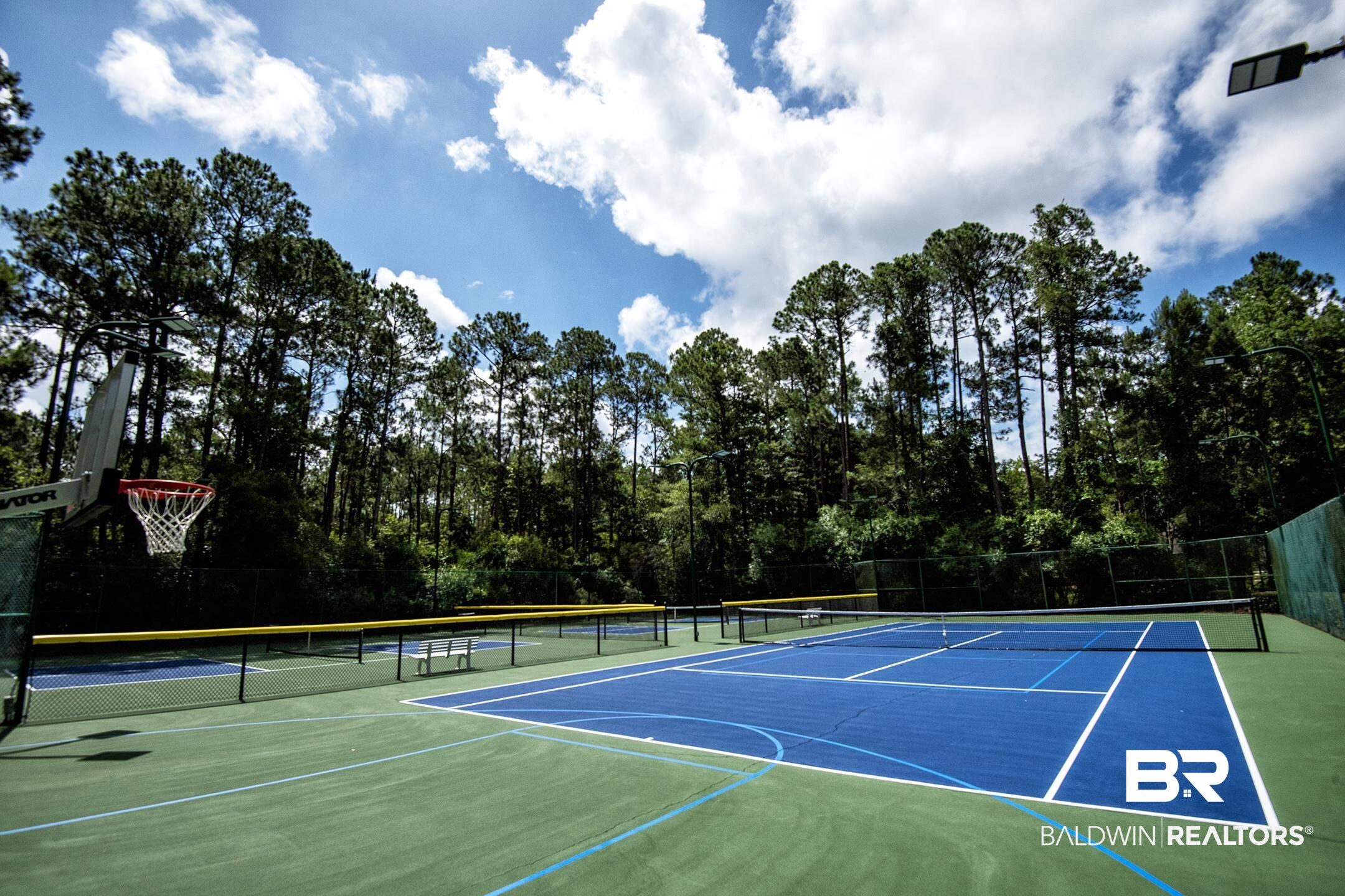 18754 Treasure Oaks Road Gulf Shores, AL 36542 - Photo 47 of 53 Multi-sport court featuring a blue tennis court surface with white lines, a basketball hoop, and green perimeter fencing