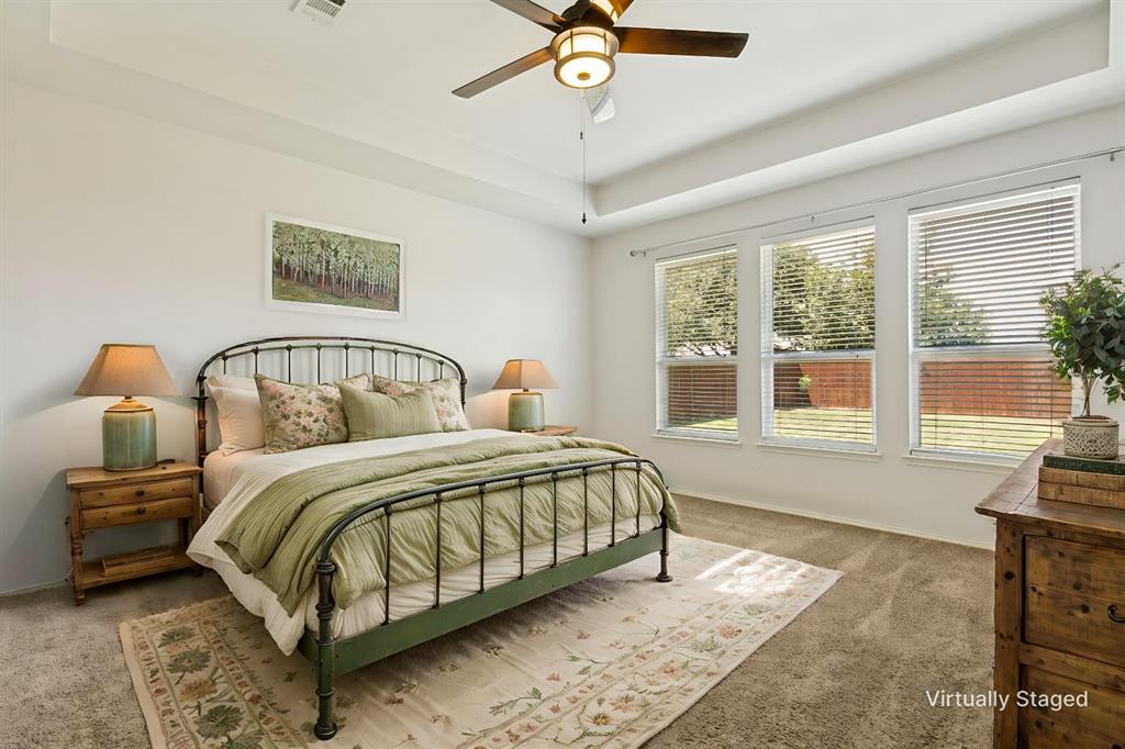 4107 Waverly Road Corinth, TX 76208 - Photo 13 of 30 The downstairs primary suite offers a restful retreat that is separated from all of the other bedrooms. With a beautiful tray ceiling, upgraded ceiling fan, and windows overlooking the backyard, this space provides for privacy and relaxation.