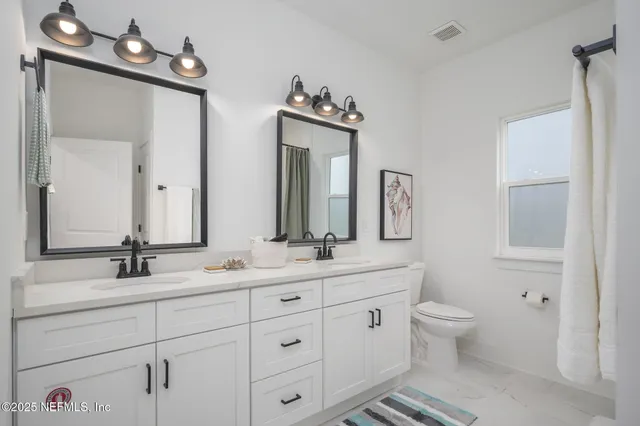 a bathroom with double vanity sinks a toilet a mirror and shower