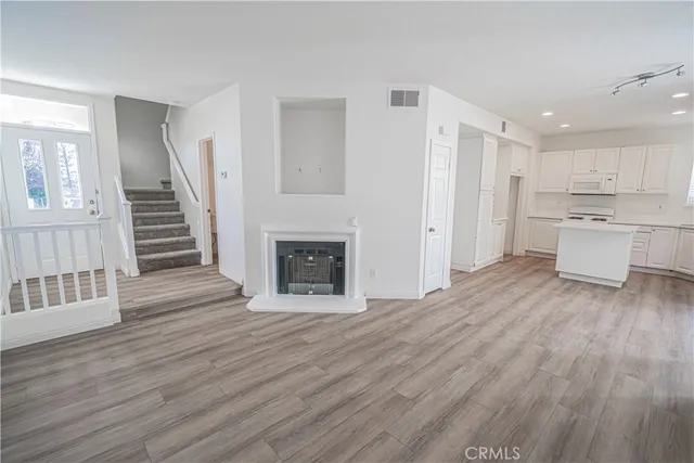 a view of a kitchen and an empty room with wooden floor and a fireplace