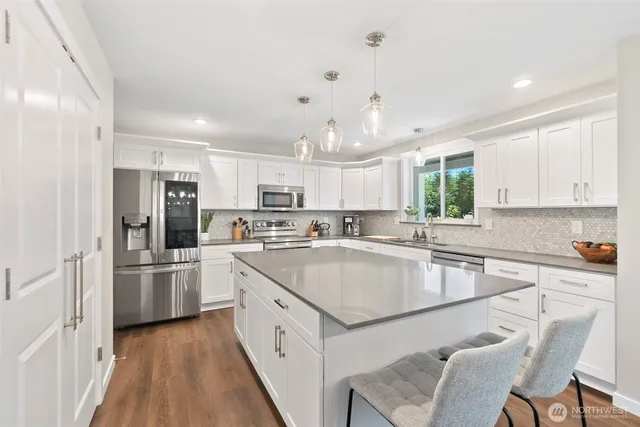 a kitchen with stainless steel appliances granite countertop a refrigerator a sink dishwasher a stove and white countertops with wooden floor