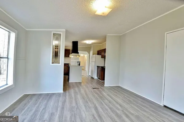 an empty room with wooden floor kitchen view and windows