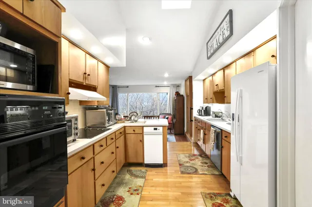 a kitchen with stainless steel appliances kitchen island granite countertop a refrigerator oven a sink dishwasher and white cabinets with wooden floor