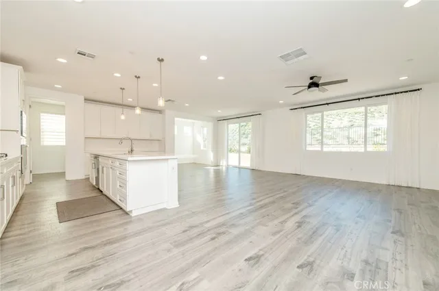 a view of an empty room and kitchen with wooden floor