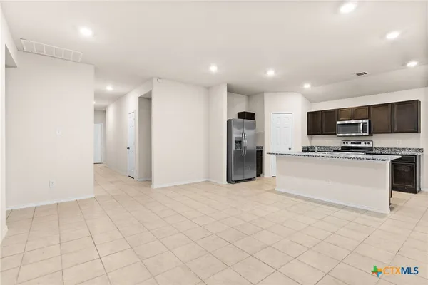 a view of kitchen with stainless steel appliances kitchen island granite countertop a refrigerator oven a sink dishwasher and white cabinets with wooden floor