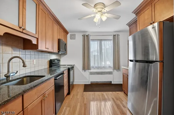 a kitchen with stainless steel appliances granite countertop a refrigerator a sink dishwasher a stove and white countertops with wooden floor