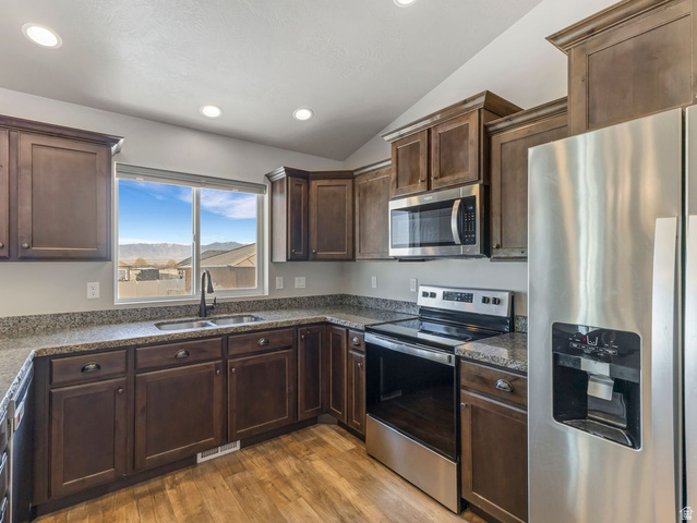 573 South Maxwell Drive Grantsville, UT 84029 - Photo 10 of 25 Kitchen featuring stainless steel appliances, dark wood finish cabinetry, dark stone countertops, light wood-style floors, and lofted ceiling