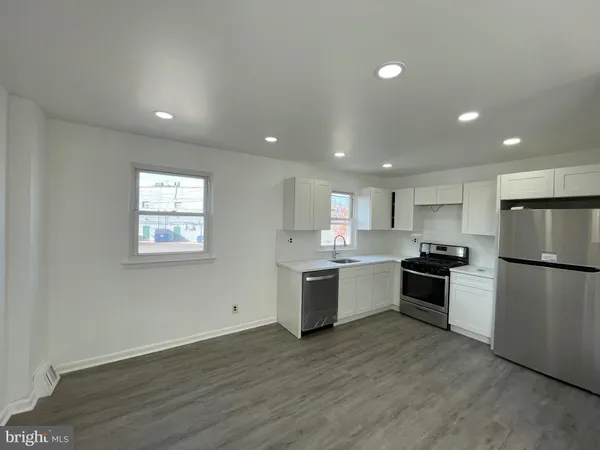 a large kitchen with a refrigerator a stove top oven a sink dishwasher and white cabinets with wooden floor