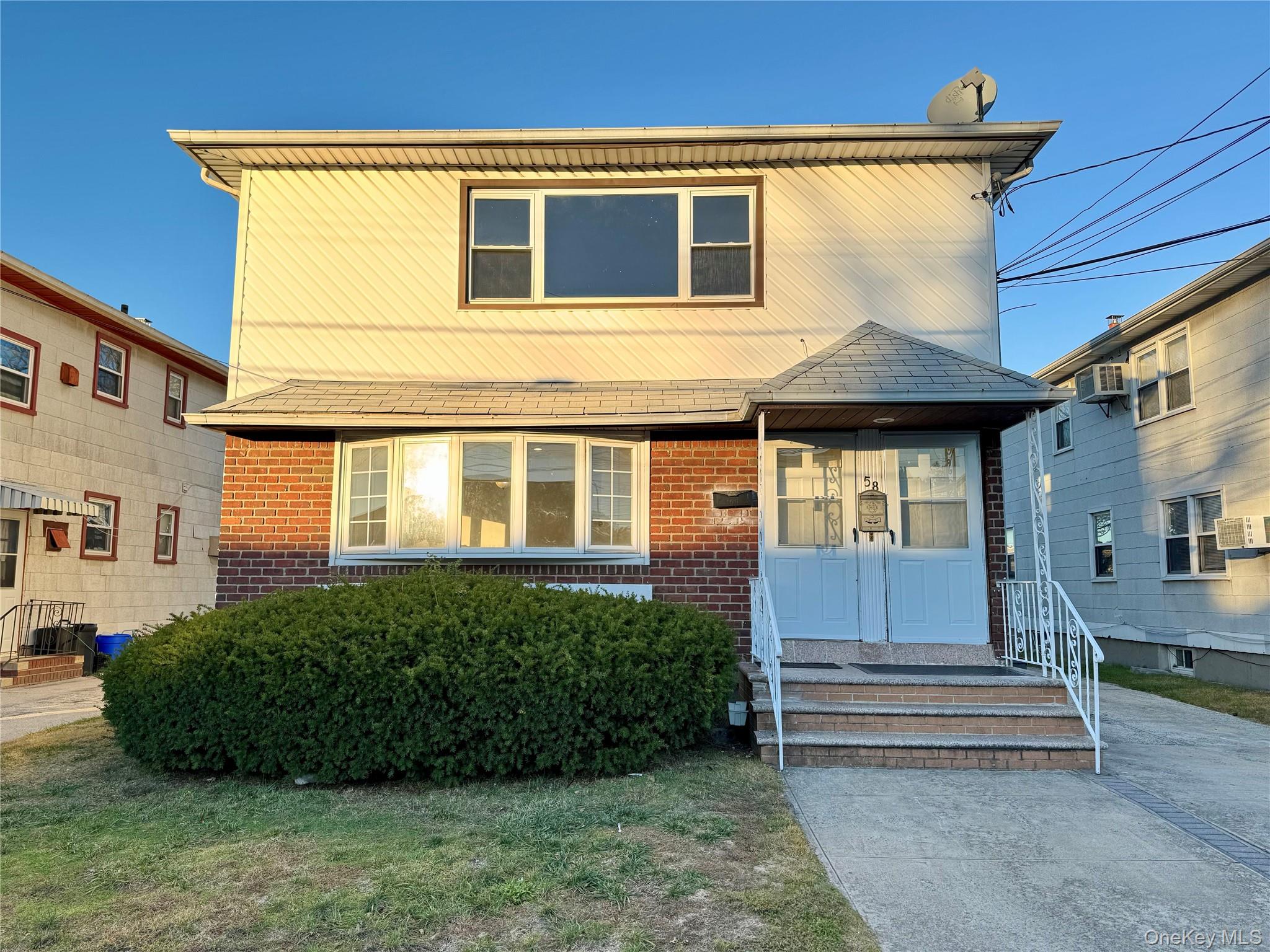 58 Cohill Road, Unit 1F Valley Stream, NY 11580 - Photo 1 of 1 Brick and siding exterior featuring a covered entry, bay window, concrete driveway, and front lawn with mature shrubbery